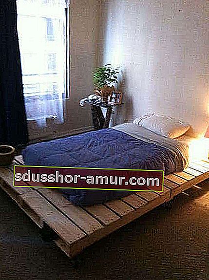 Krevet sa sirovom drvenom bazom na paletama i noćnom lampom