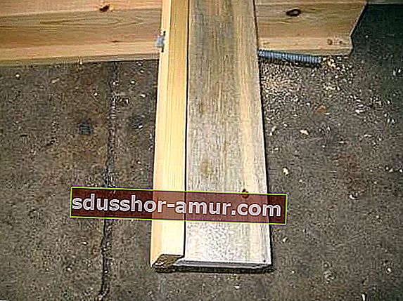 Стяжной винт, который пересекает 2 деревянные доски, собранные в Т-образной форме, на бетонном полу.