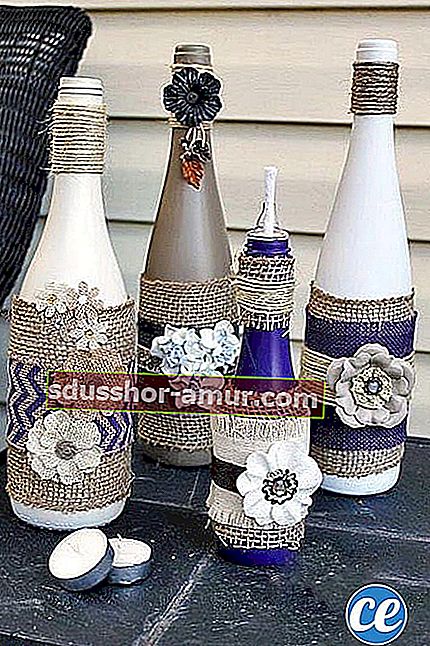 Nekoliko vinskih boca ukrašenih ljubičastom i bijelom bojom na kojima je nekoliko cvjetova 