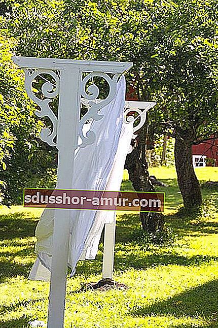 Staromodni bijeli oslikani konopac za rublje s rezbarenim drvetom u vrtu za sušenje plahte.