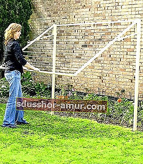 Женщина использует выдвижную сушилку, которая хранится в вертикальном положении в саду.