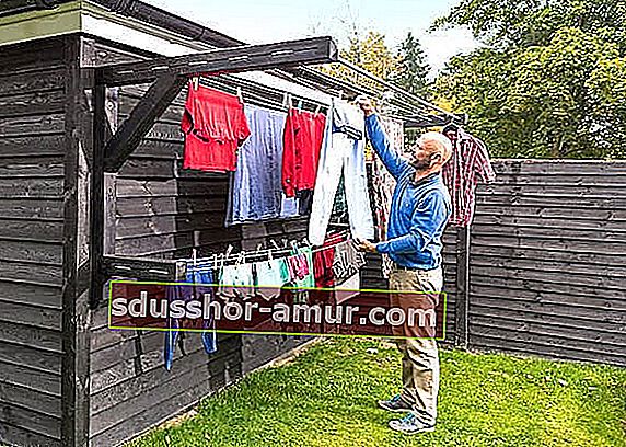 Čovjek koji suši odjeću u vrtu na drvenom zidnom nosaču odjeće.