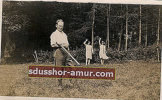 Мъж на трева с мистериозен предмет на ръката и две млади момичета, които махат зад него