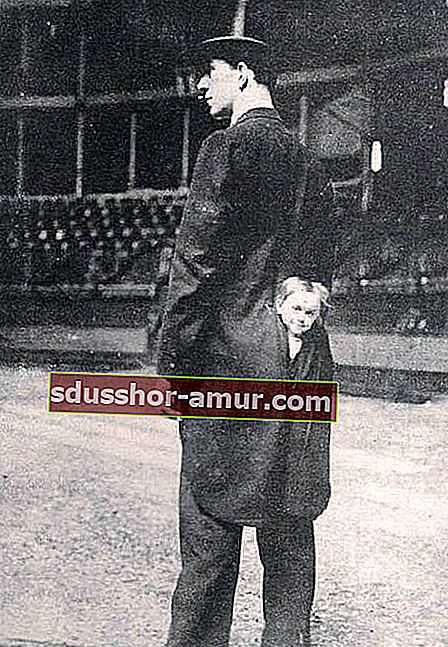 Мъж с дълго черно сако и малко момиче, издаващо глава от задната част на сакото 