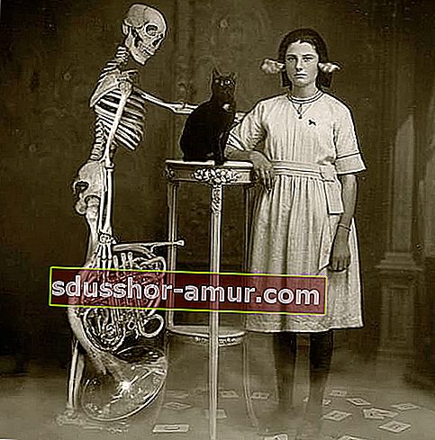 Скелет, държещ инструмент с черна котка пред себе си и жена, облечена в бяло с хартия в ушите 
