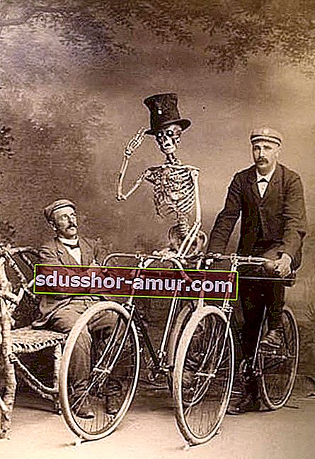 Скелет на велосипеде рядом с двумя мужчинами, один сидит, а другой на другом велосипеде 