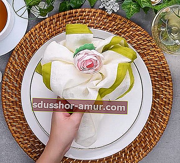Presavijena salveta u obliku buketa cvijeća postavljena na bijeli tanjur