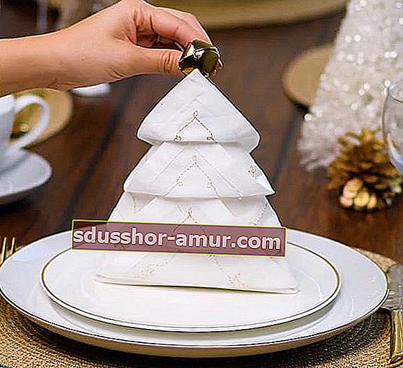Bijela salveta savijena u božićno drvce i stavljena na bijeli tanjur