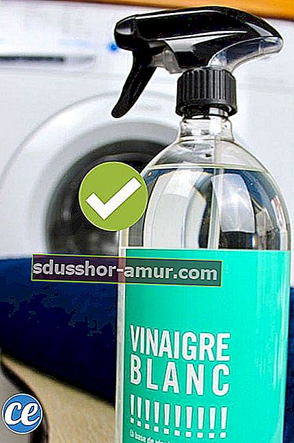 O sticlă de spray cu oțet alb în fața unui prosop albastru și a unei mașini de spălat.