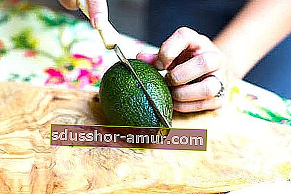Авокадо, лежащо на масата, което се разрязва наполовина с нож