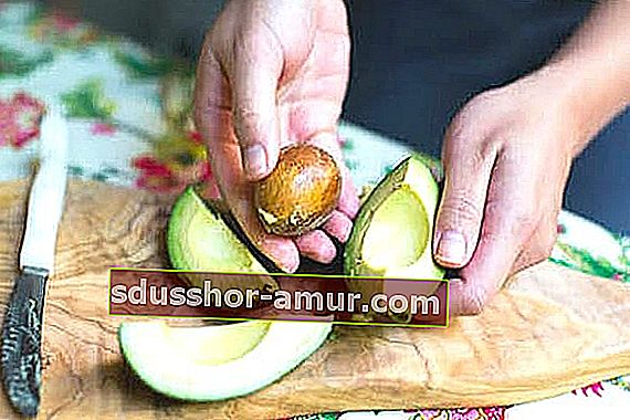 Uklonjena jezgra avokada u ruci i tri četvrtine avokada na stolu