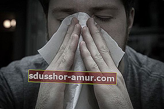 Човек, който издухва носа си с кърпичка заради алергии