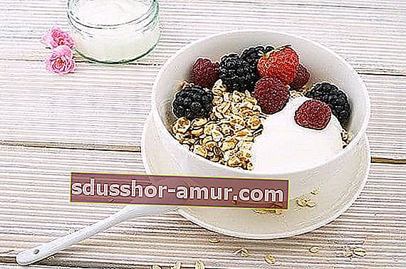 Bijela zdjela zobenih pahuljica s jogurtom i drvenim jagodama i žlicom koja leži na drvenom stolu