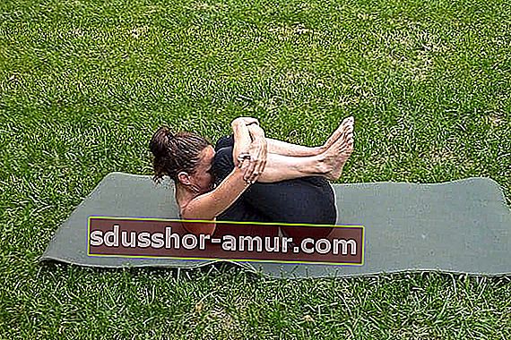 йога поза за освобождаване на вятъра с жена в черни чорапогащи на тревата